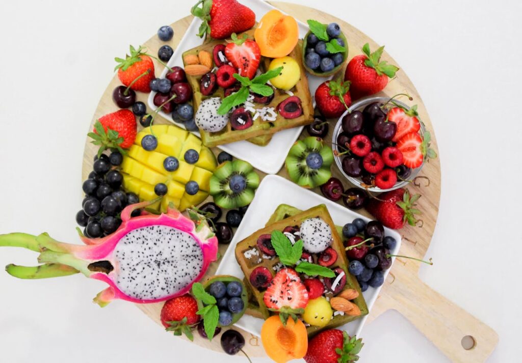 Colorful assortment of fresh fruits including strawberries, blueberries, dragon fruit, mango, and kiwi arranged on a wooden platter, showcasing a vibrant, healthy snack ideal for plant-based living and nutrition.